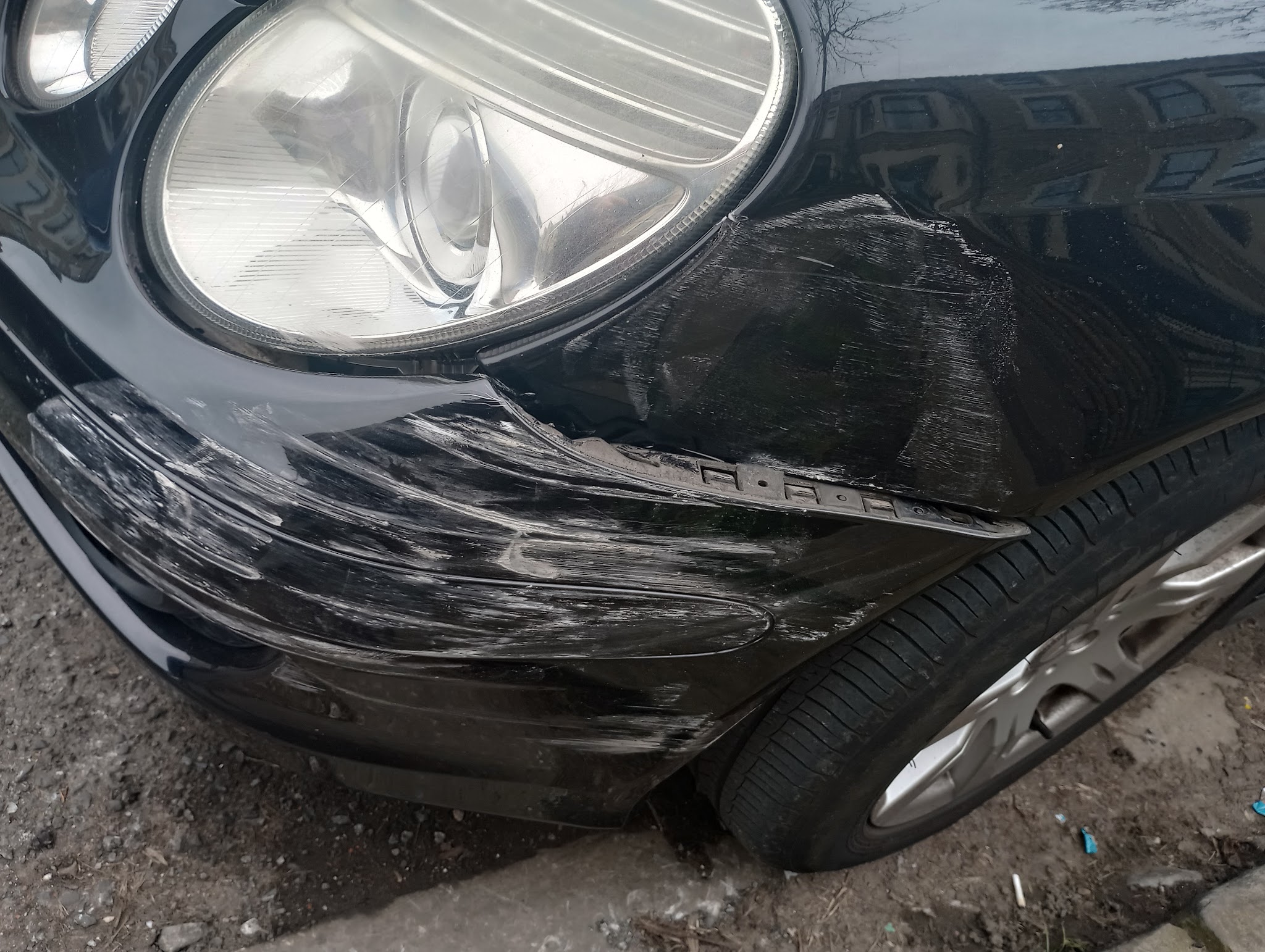 Black car with heavy scuffs and scratches across the front wing and bumper